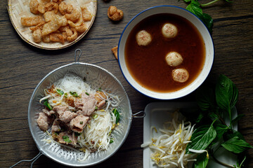 A rustic wooden table holds a steaming bowl of Thai noodle soup, ready to be enjoyed.