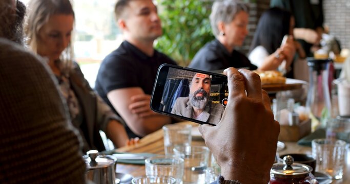 Blogger recording feedback about event using smartphone, sitting at table in casual atmosphere. Concept content creation, storytelling, sharing opinions for social media audience. Blogger Concept