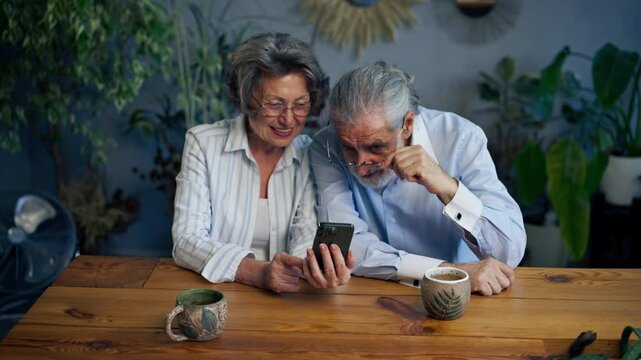 elderly people sitting at a table together watching social networks on the phone funny videos happy old age elderly couple pleasant memories leisure time in old age warm feelings support in old age
