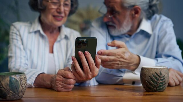 elderly people sitting at a table together watching social networks on the phone funny videos happy old age elderly couple pleasant memories leisure time in old age warm feelings support in old age