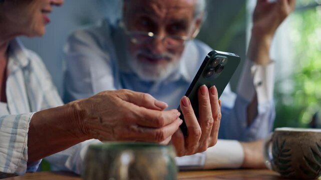 close up elderly people sitting at a table together watching social networks on the phone funny videos happy old age elderly couple pleasant memories leisure time in old age warm feelings support in