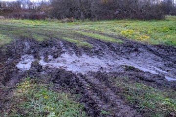 Fototapeta premium puddles in tractor tire traces in green meadow. Country road in bad condition.