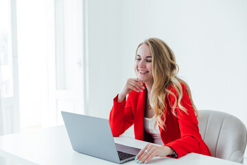 blonde woman in red business suit with laptop online in office at desk