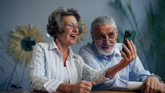 elderly people sitting at a table together watching social networks on the phone funny videos happy old age elderly couple pleasant memories leisure time in old age warm feelings support in old age