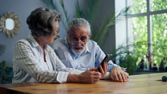 elderly people sitting at a table together watching social networks on the phone funny videos happy old age elderly couple pleasant memories leisure time in old age warm feelings support in old age