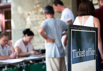 A sign for a ticket office to the museum, people are standing in blurred focus, selective focus