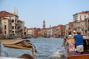 Rear view of group of tourists sailing on tour boat on Grand Canal next to Church of San Bartolomeo di Rialto in a sunny summer day in Venice. Soft focus. Copy space. Travel in Italy theme. © Андрей Рыков
