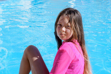 Happy teenage girl with loose, tangled hair from the wind sitting on the background of blue water, acne on the girl's forehead, selective focus