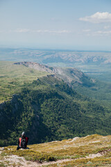 Male tourist resting and looking at the forest from the top of a mountain on a hike