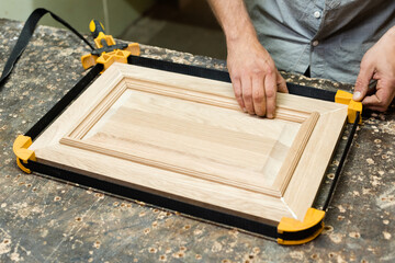 The carpenter tightens the tape clamp and checks the tightening of the oak panel