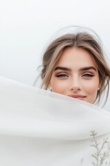 Fototapeta premium Portrait of a bride with soft makeup and windswept hair holding a sheer veil