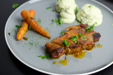 Roasted pork belly with glazed carrots and cauliflower puree in a grey plate