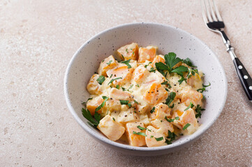 Bowl of pumpkin in sour cream sauce sprinkled with fresh parsley on beige textured stone table. Vegetarian food