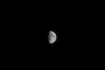 a large crescent moon illuminated against a stark, dark night sky. The surface of the moon is visible with various textures and craters, creating a detailed appearance.
