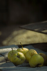 several yellow apples or quince fruits placed on a textured surface, likely a wooden board or stone. The apples appear slightly speckled, suggesting they are not perfectly polished