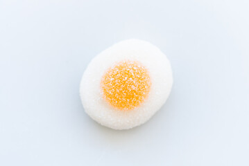 View from above of a fried egg made of jelly beans with sugar on top. It is on a clean white background. Concept of sweet eating, indulgence and excess sugar
