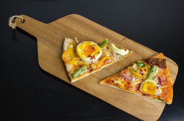 Slice of homemade vegetarian pizza with eggs, beans and sun dried tomatoes on a wooden  board on a black table
