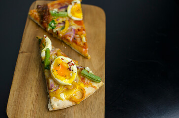 Slice of homemade vegetarian pizza with eggs, beans and sun dried tomatoes on a wooden  board on a black table