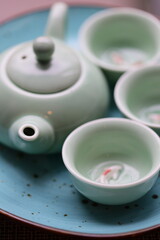 A tea pot with four cups on a plate, ready for serving.