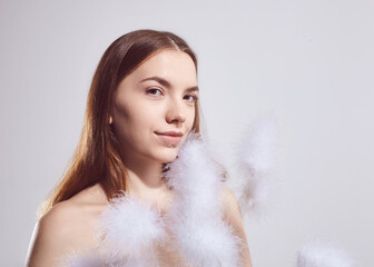 A beautiful brunette woman with fluffy plants in her hands poses on a light background....