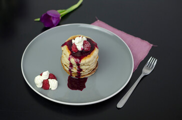 Stack of American pancakes with dripping blueberry jam and fresh raspberries
