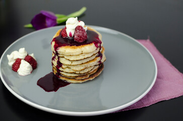 Stack of American pancakes with dripping blueberry jam and fresh raspberries