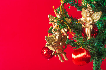 Golden angel ornaments and red baubles on a Christmas tree with a red background