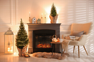 Small spruce trees decorated with Christmas lights near fireplace indoors