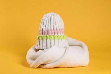 Stylish knitted hat and warm scarf on yellow background