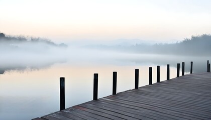 Naklejka premium Tranquil lakeside wooden boardwalk in misty morning light.