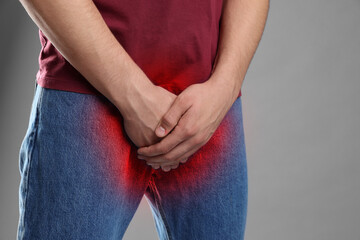 STD (sexually transmitted diseases). Man holding hands near his groin on grey background, closeup....