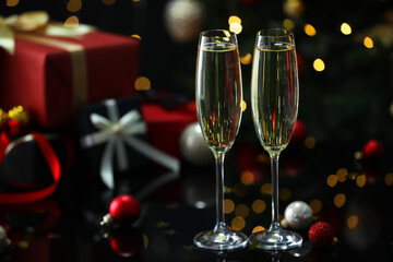 Delicious champagne in glasses and Christmas decor on black mirror surface against blurred lights, closeup. Space for text