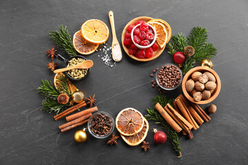 Frame of different aromatic spices and fir tree branches on black table, flat lay. Christmas season