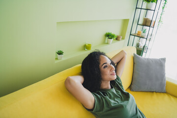 Portrait of nice young girl sitting sofa hands behind head imagine green interior living room flat...