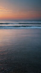 Obraz premium Long exposure of ocean at sunset with soft pink, white, and blue hues.