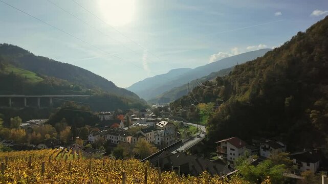 Scenic aerial footage of Klausen in the Eisack Valley, South Tyrol. Features golden vineyards, charming alpine architecture, and the Brenner Autobahn with a backdrop of stunning mountain scenery.