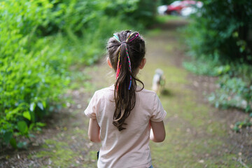 A cute little girl with dreadlocks is walking with a dog on a leash in the summer. The concept of a cheerful active carefree child