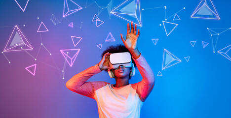 African girl with VR glasses standing at blue and pink background and looking at floating geometric...