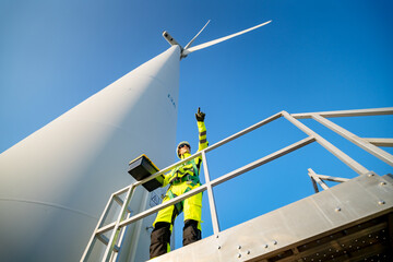 A group of workers in high-visibility gear joyfully high-fives each other after completing their tasks at a wind farm, surrounded by lush greenery and turbine blades spinning in the background.