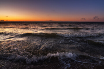 waves with breakers in stormy weather in a large raging lake in the warm light of the evening dawn. picturesque surf close-up, side view from below