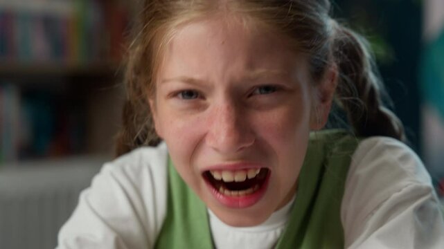 Mad furious Caucasian little girl school child kid schoolgirl angry naughty teenage learner student pupil screaming shouting yell anger irritated emotion education looking at camera indoors classroom