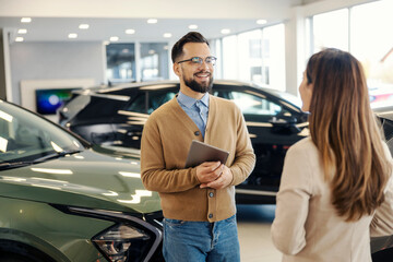 Car seller with tablet talking to a customer at car salon.