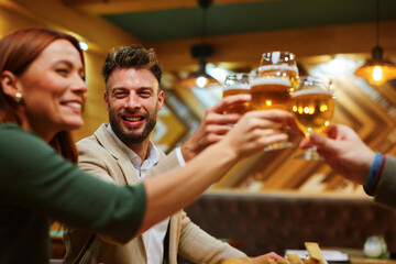 Happy friends are toasting with beer glasses enjoying a cheerful moment together in a restaurant