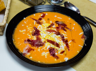 Salmorejo - tomato soup puree with bread traditionally served cold with jamon and boiled egg in black bowl. Andalusian cuisine..