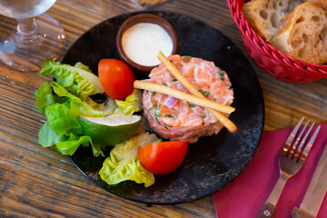 French style starter of salmon tartare with creamy chive sauce and vegetable garnish of fresh lettuce, tomato, lime and crispy breadsticks