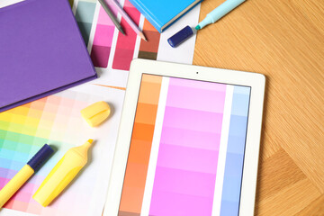 Designer's workplace with tablet, palettes and stationery on wooden table, top view