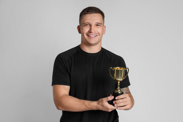 Happy winner with golden trophy cup on light grey background