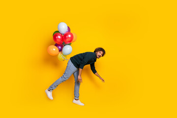 Young man with colorful balloons against bright yellow background, wearing black shirt and jeans, mixed race student