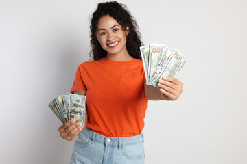 Happy woman with dollar banknotes on light grey background