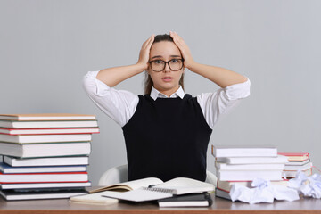 Young student having stress before exam at desk against grey background